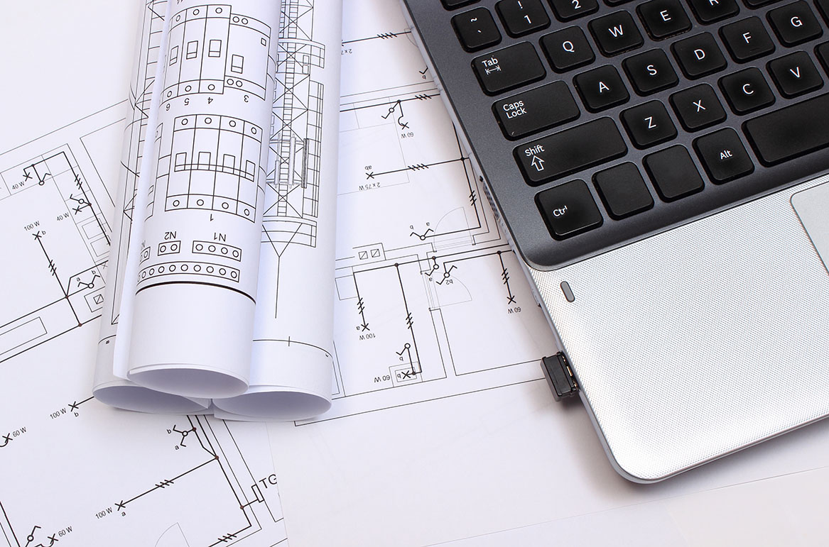 Electrical engineering blueprints and schematics displayed beside a laptop for commercial electrical system design.